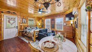 A cozy log cabin interior with a bed, a dining table set for two, and a ceiling fan. - Romantic Hot Tub Cabin w/ Fast WiFi | Near Smokies (Sevierville)