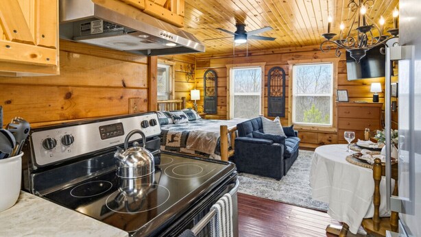 A cozy cabin-style room with a kitchen area, a dining table, and a sofa. - Romantic Hot Tub Cabin w/ Fast WiFi | Near Smokies (Sevierville)