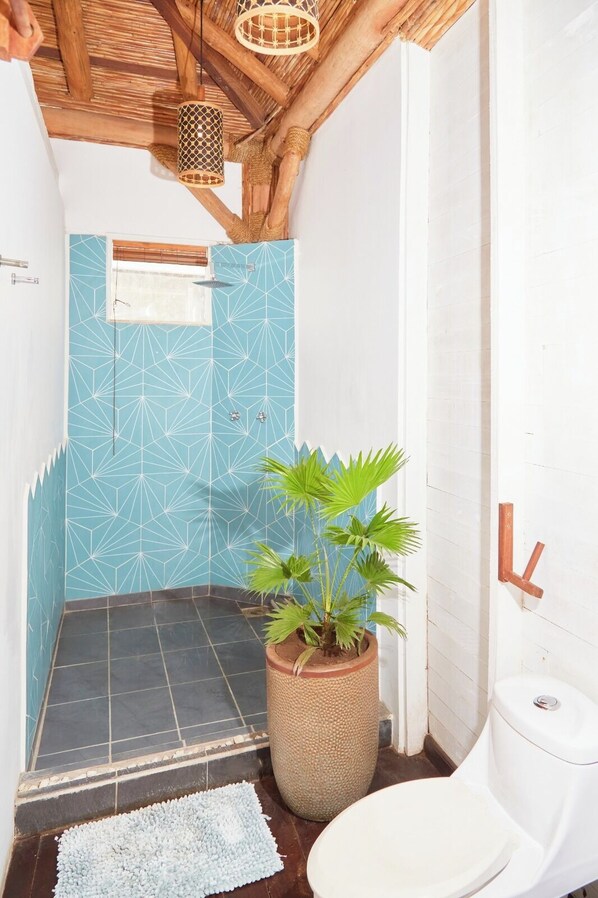 Et badeværelse med geometrisk flisevæg, en potteplante, en bruser og et toilet.
