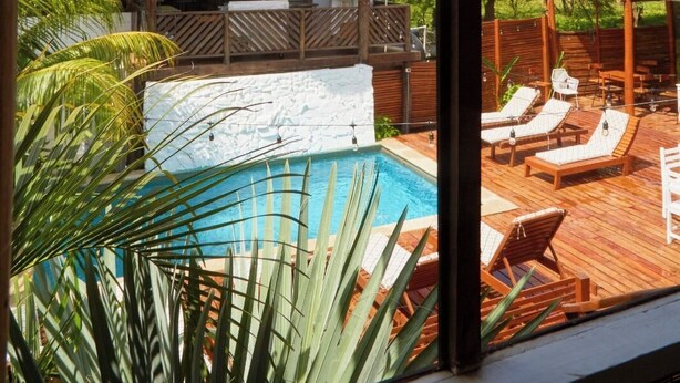 A pool area with lounge chairs, a thatched-roof structure, and lush greenery. - Sohla Beach Hotel popoyo (Jiquelite)