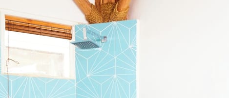 A bathroom with a geometric tile pattern, a window with blinds, and a wooden ceiling structure.