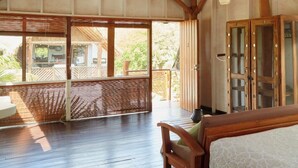A spacious room with a wooden ceiling and floor, large sliding glass doors leading to an outdoor area, and a bed with a patterned bedspread. - Sohla Beach Hotel popoyo (Jiquelite)