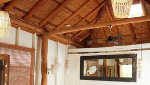 A spacious room with a high wooden ceiling, a large bed with white linens, a wooden sofa with green cushions, and a wooden table with a vase. - Sohla Beach Hotel popoyo (Jiquelite)