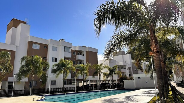 A modern apartment complex with a swimming pool, palm trees, and a clear blue sky. - PCM402VG21 (Florianópolis)