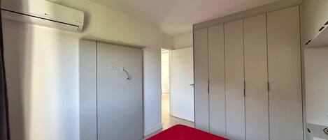 Une chambre avec une couvre-lit rouge, une armoire blanche et un appareil de climatisation.
