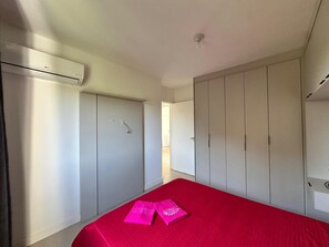 Une chambre avec une couvre-lit rouge, une armoire blanche et un appareil de climatisation.