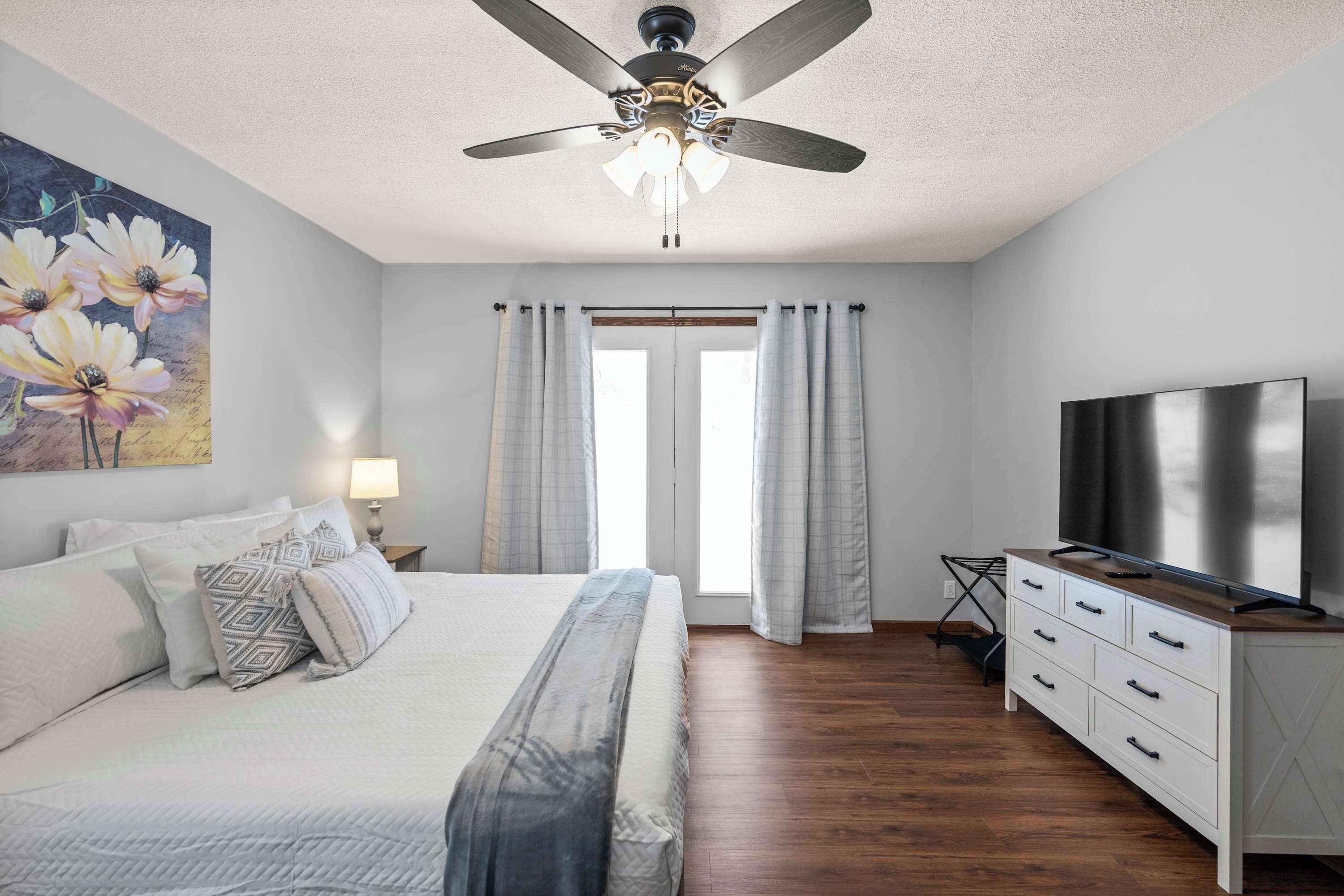 A bedroom with a bed, a ceiling fan, a TV, and a window with curtains.