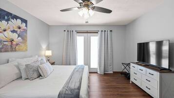 A bedroom with a bed, a ceiling fan, a TV, and a window with curtains.