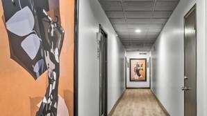 A hallway with a wooden floor, a large abstract painting on the left, and a door on the right.