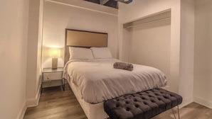 A bedroom with a bed, bedside table, lamp, and a bench.