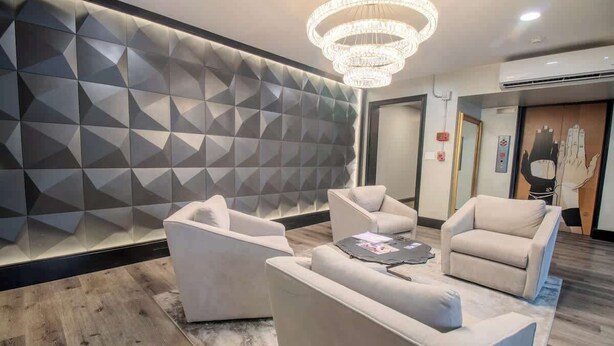 A modern lobby with a geometric patterned wall, a chandelier, and a seating area with sofas and a coffee table.