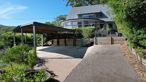 A covered outdoor area with a concrete floor, surrounded by greenery and a house in the background. - Bay views with a secluded bush backdrop (HARDYS BAY)
