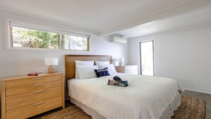 A bedroom with a large bed, wooden nightstands, a window with blinds, and a view of greenery outside. - Bay views with a secluded bush backdrop (HARDYS BAY)