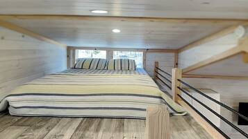 Une chambre confortable située dans les combles, avec un lit superposé en bois, une couvre-lit à rayures et une vue par la fenêtre.