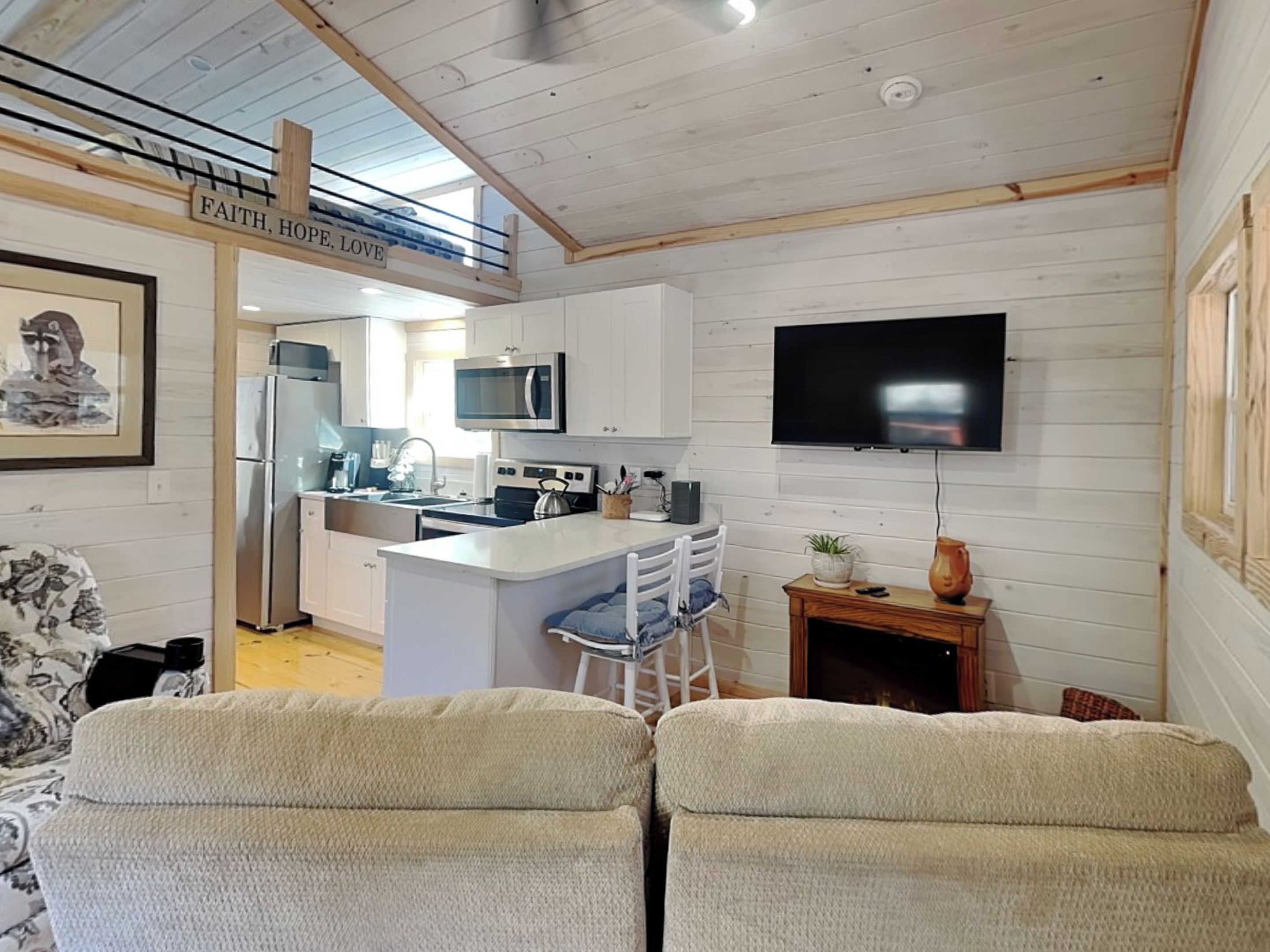 Una cocina moderna con armarios blancos, una isla central y un televisor de pantalla plana montado en la pared.