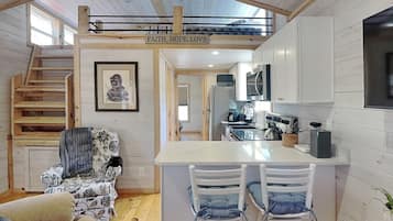 Una cocina compacta con una isla central, un comedor con dos sillas, una escalera y un cuadro en la pared.