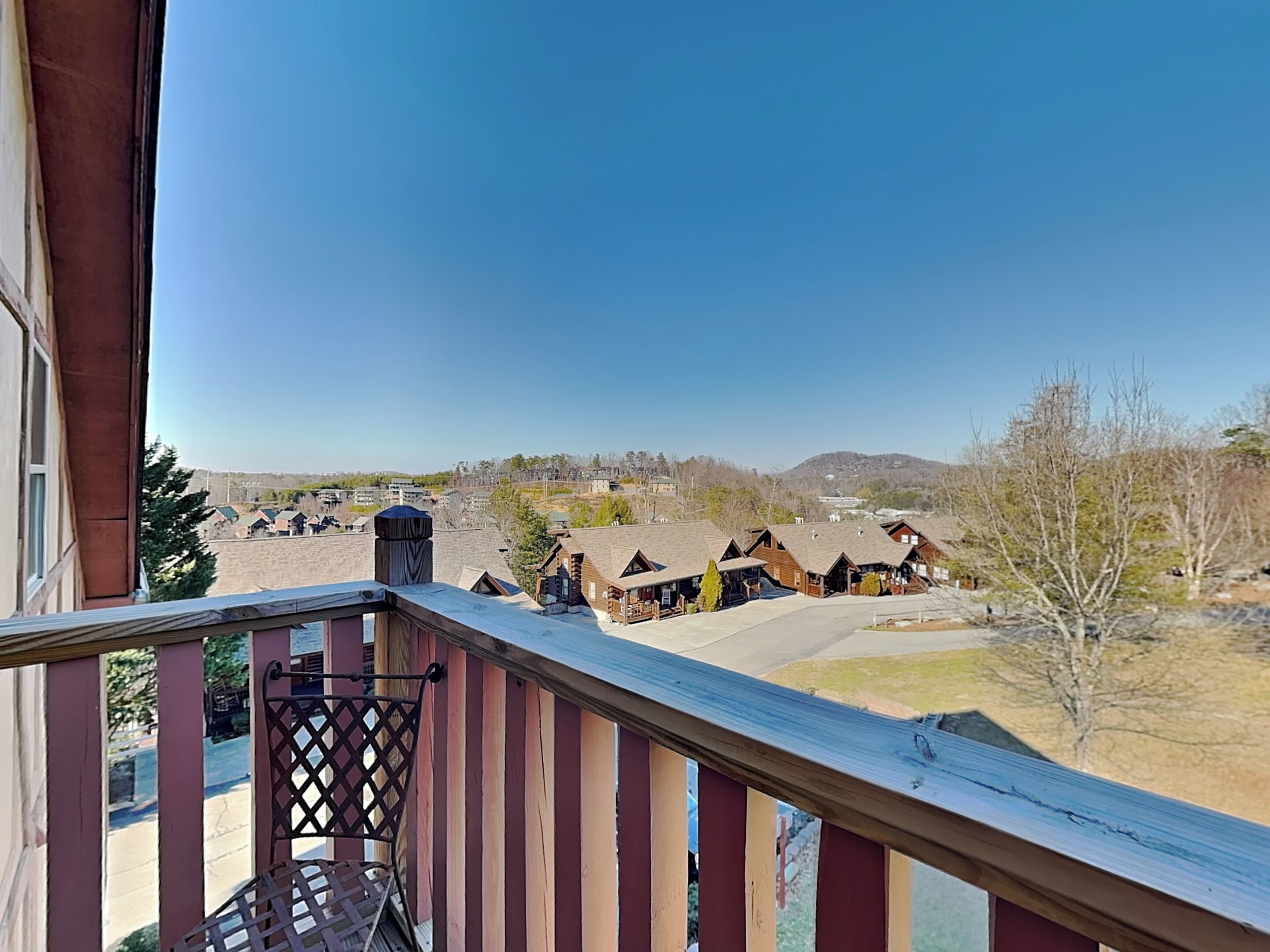 A balcony with a view of a residential area, including houses and a hilly landscape.
