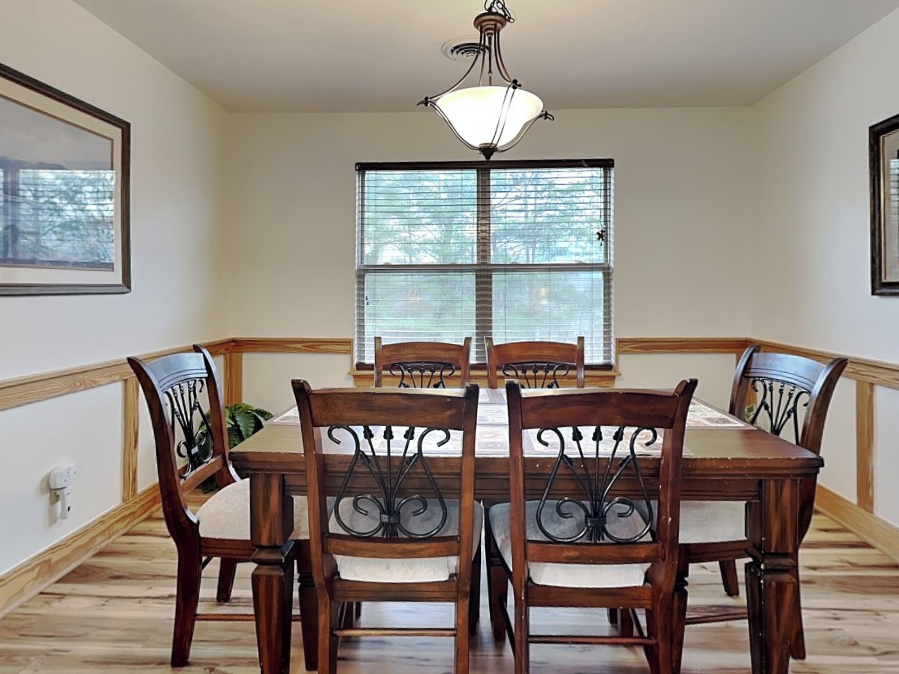 A dining room with a wooden table and chairs, a chandelier, and a window with blinds.