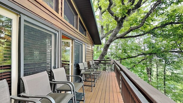 Eine Holzterrasse mit Sitzgelegenheiten im Freien, großen Fenstern und Blick auf Bäume.