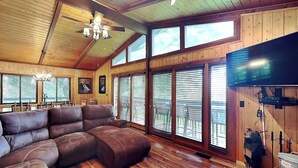Ein geräumiges Wohnzimmer mit einer grossen Eckcouch, Holzböden, einem Deckenventilator und grossen Fenstern.