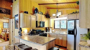 Eine Küche mit Holzausbau, einer Granit-Arbeitsplatte, einem Edelstahlkühlschrank und einer zentralen Kochinsel mit Barhocker.