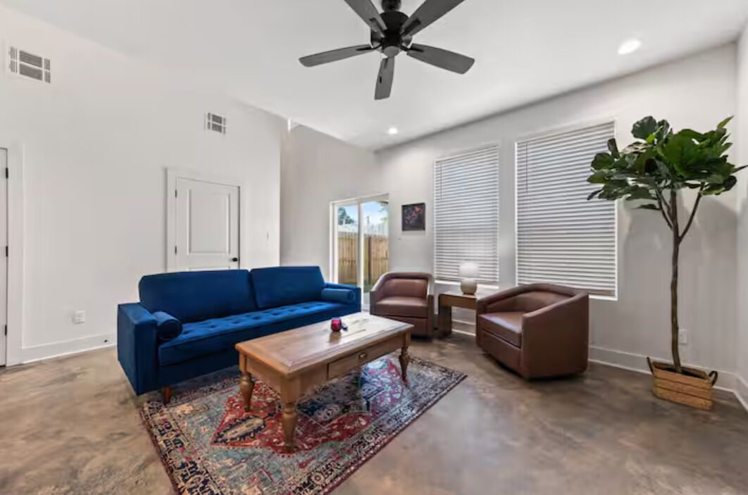 Una sala de estar con un sofá azul, una mesa de centro de madera, un sillón de cuero marrón y una planta en maceta.