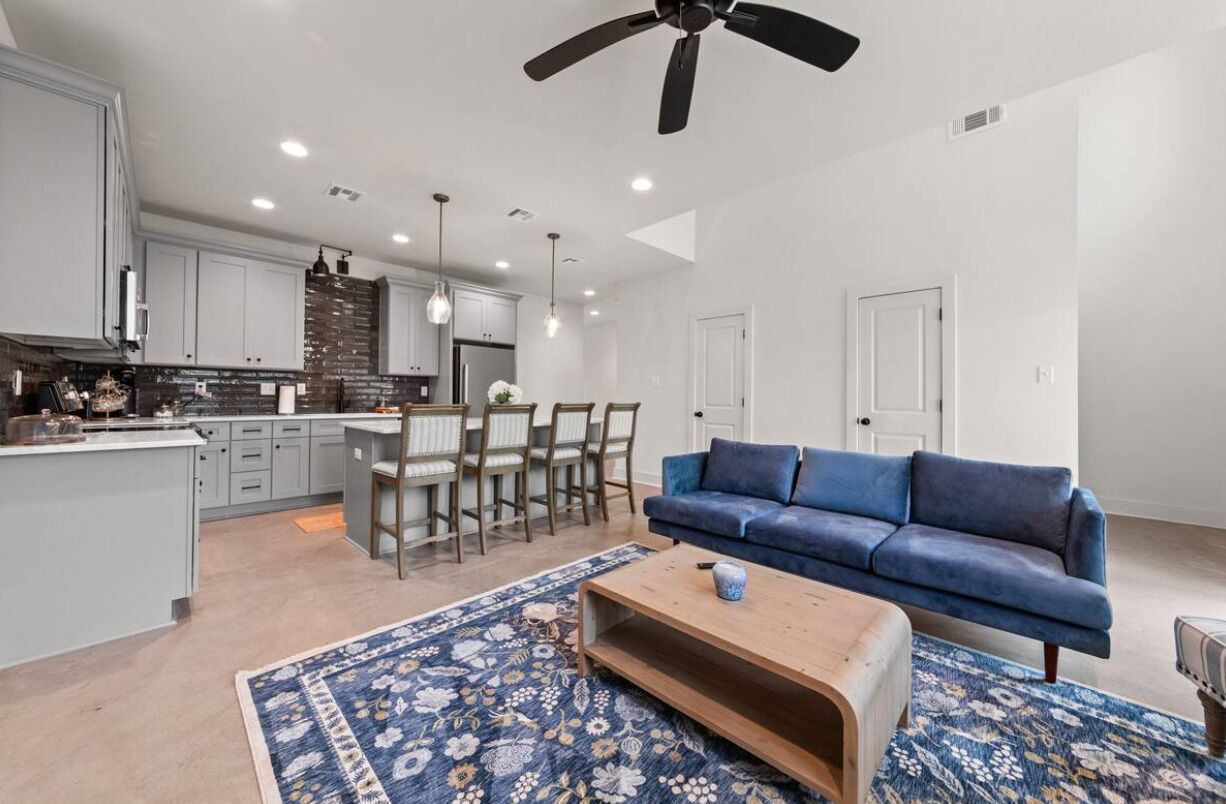 A modern kitchen with grey cabinets, a dining area with a blue sofa, and a ceiling fan.