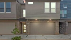A modern two-story residential building with a garage, a small front yard, and a clear sky.