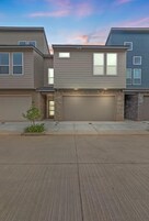 A modern two-story residential building with a garage, a small front yard, and a clear sky.