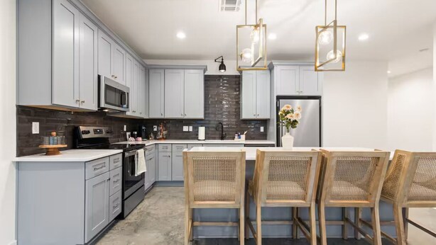 A modern kitchen with grey cabinets, a central island with a sink, and a dining area with wicker chairs.