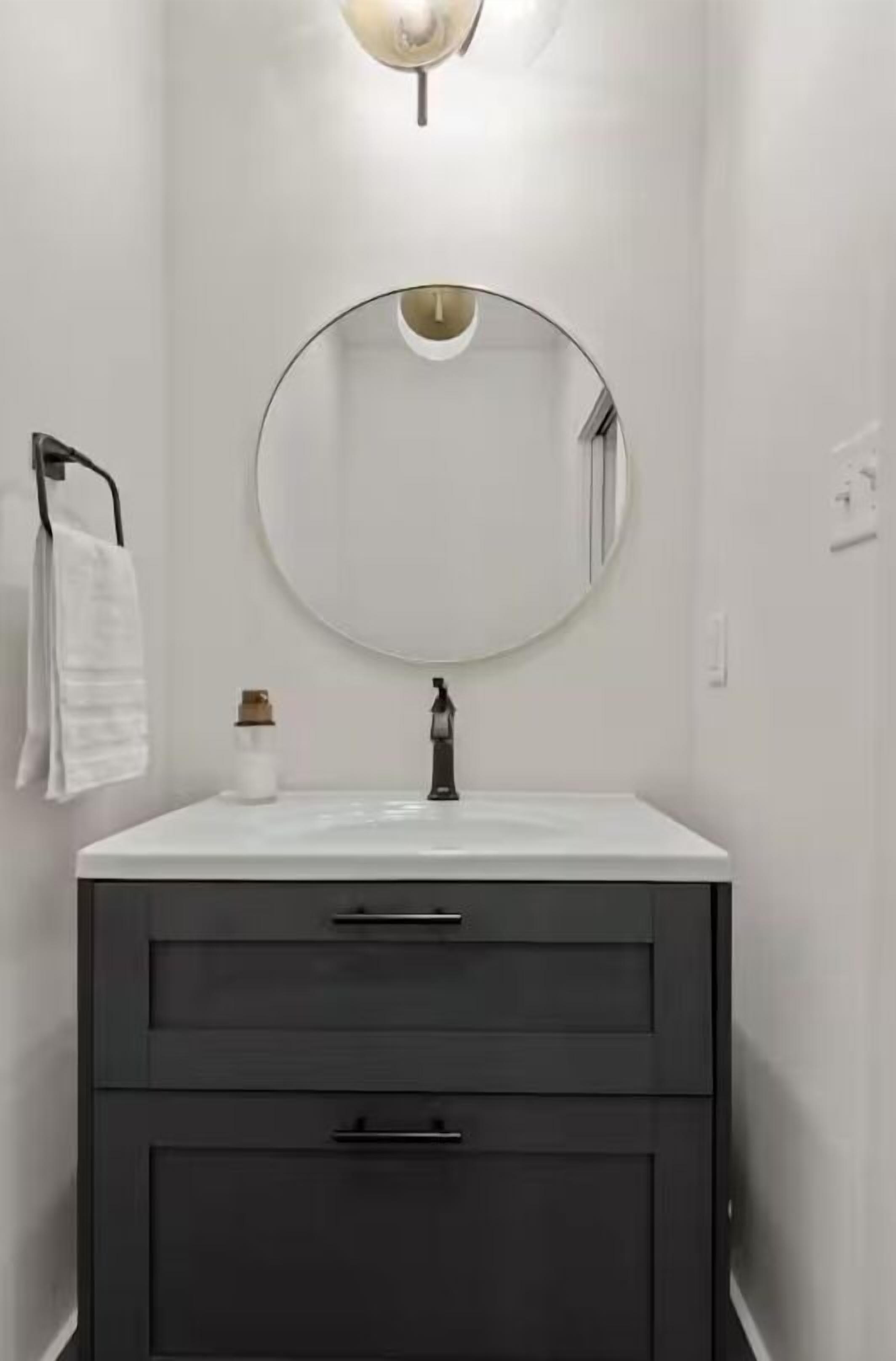 A bathroom with a white vanity, a round mirror, and a towel hanging on a rack.