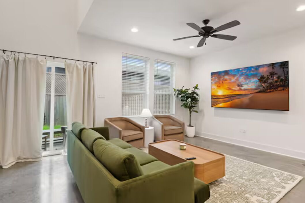 A modern living room with a green sofa, two armchairs, a coffee table, and a ceiling fan.