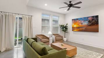 A modern living room with a green sofa, two armchairs, a coffee table, and a ceiling fan.