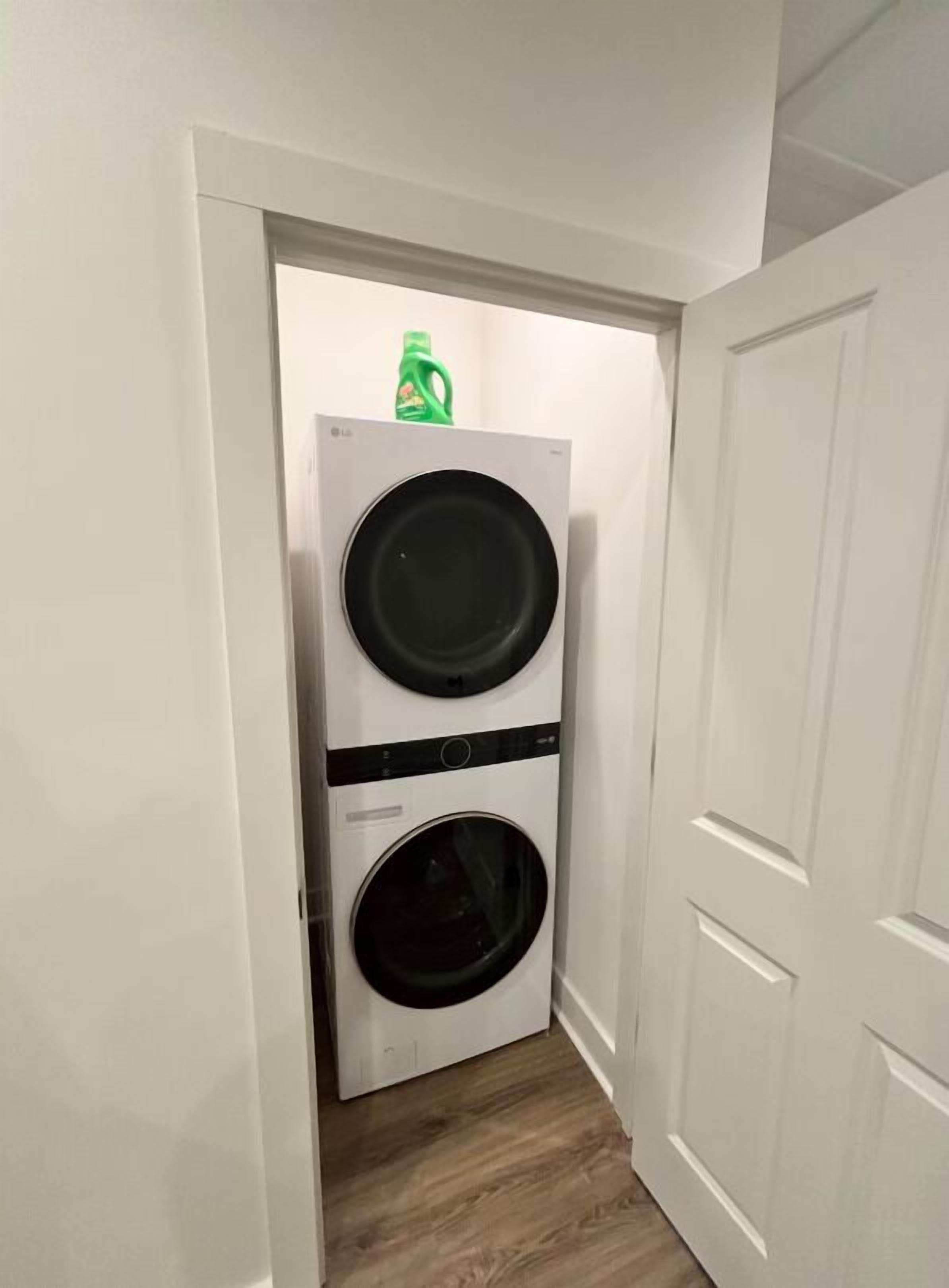 Un lavadero con dos lavadoras apiladas y una botella de detergente verde encima.