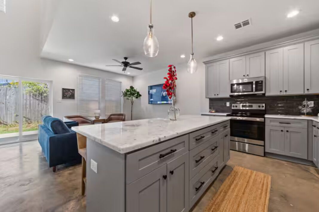 A modern kitchen with grey cabinets, stainless steel appliances, and pendant lighting.