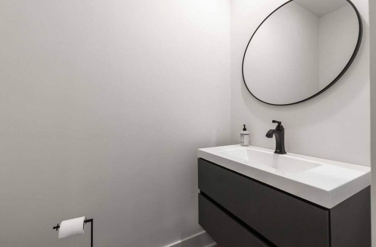 Une salle de bain moderne avec un lavabo blanc, un robinet noir et un miroir rond.