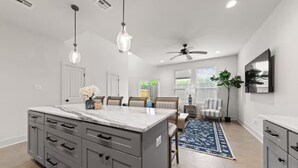 A modern kitchen with a marble island, grey cabinetry, and pendant lighting.