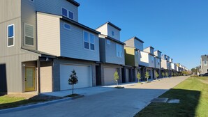 A row of modern townhouses with attached garages, a clear sky, and a well-maintained lawn.