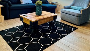 Ett vardagsrum med en mörkblå soffa, en grå fåtölj, ett soffbord i trä och en svartvit, hexagonformad matta.