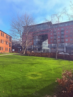 A grassy courtyard with a modern building featuring large windows and a red facade. - Victoria Court • Stay Angels (Broomhall)