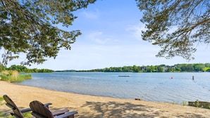 Une vue sur le lac, avec une plage de sable, des chaises en bois et une jetée où est amarré un bateau.