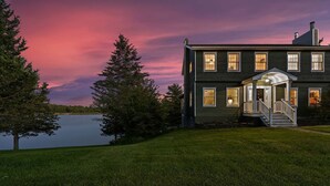 Une maison à deux étages avec un porche, un lac et des arbres.