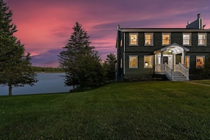 A two-story house with a porch, a lake, and trees. - Lakefront Luxe Retreat | Beach, Pools, Pickleball (Athens)