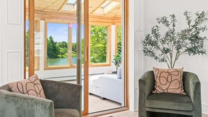 Une pièce dotée d’une porte-fenêtre coulissante qui donne sur un espace extérieur offrant une vue sur la verdure et un plan d’eau. On y trouve deux fauteuils ornés de coussins à motifs.