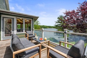 Una terraza con asientos al aire libre, una mesa con una bebida y vista a un lago.