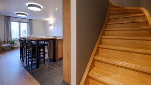 Un intérieur moderne avec un escalier en bois, un coin repas comprenant une table et des chaises, et une vue par la fenêtre.