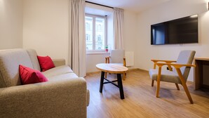 Un salon moderne comprenant un canapé, deux fauteuils, une petite table en bois, un téléviseur à écran plat et une fenêtre avec des rideaux.