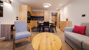 Une cuisine moderne avec des meubles en bois, un coin repas doté d’une table ronde et un salon avec un canapé et des fauteuils.