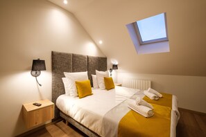Un dormitorio moderno con una cama grande, dos mesitas de noche, un ventanal pequeño y una lámpara de pared.