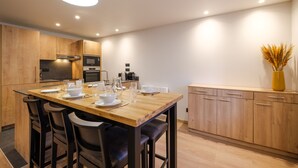 A modern kitchen with wooden cabinets, a wooden dining table with chairs, and a built-in oven. - Grand T3 familial en centre-ville (Lons-le-Saunier)